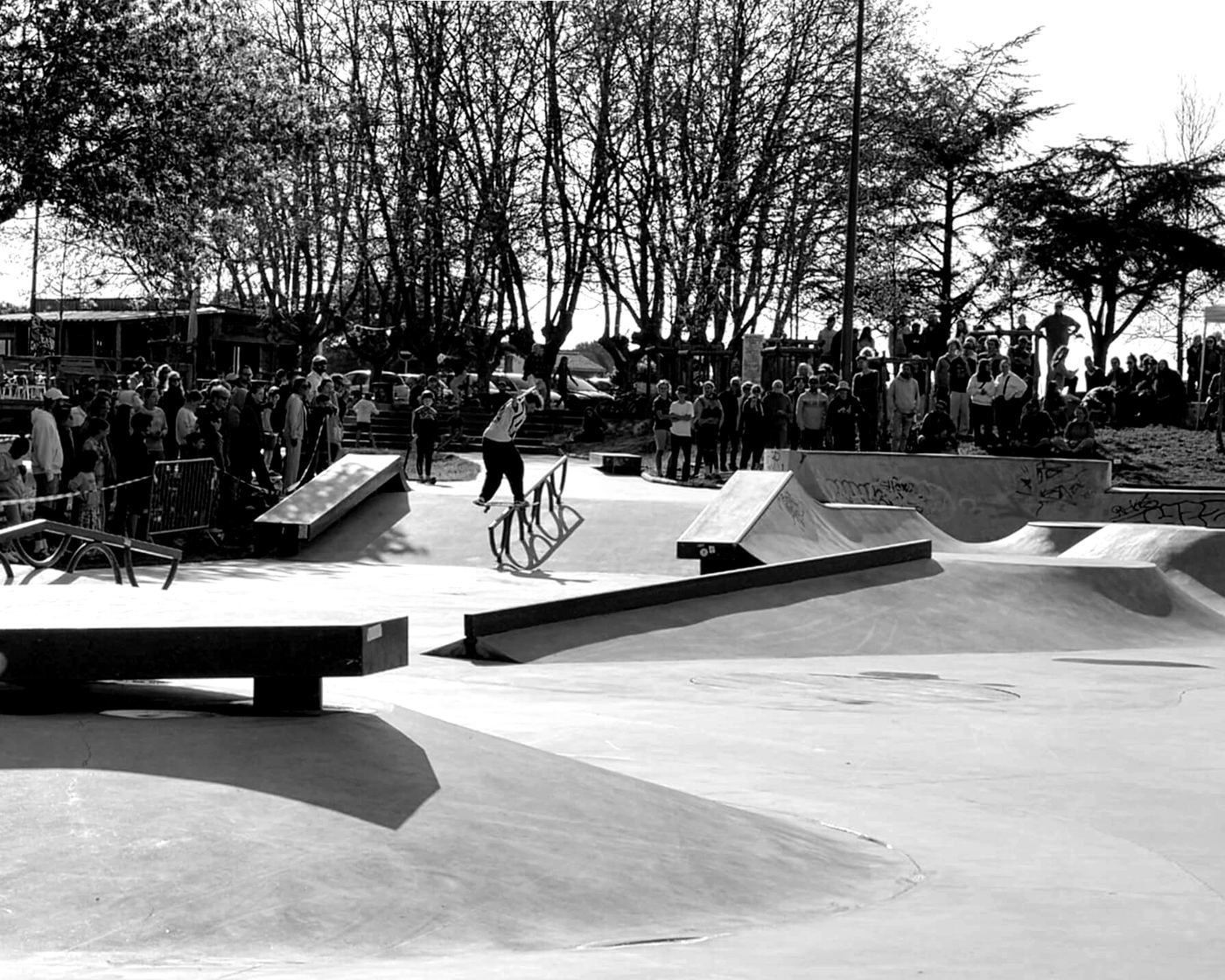Un skater glisse sur un rail pendant un contest, le public massé autour du skatepark.